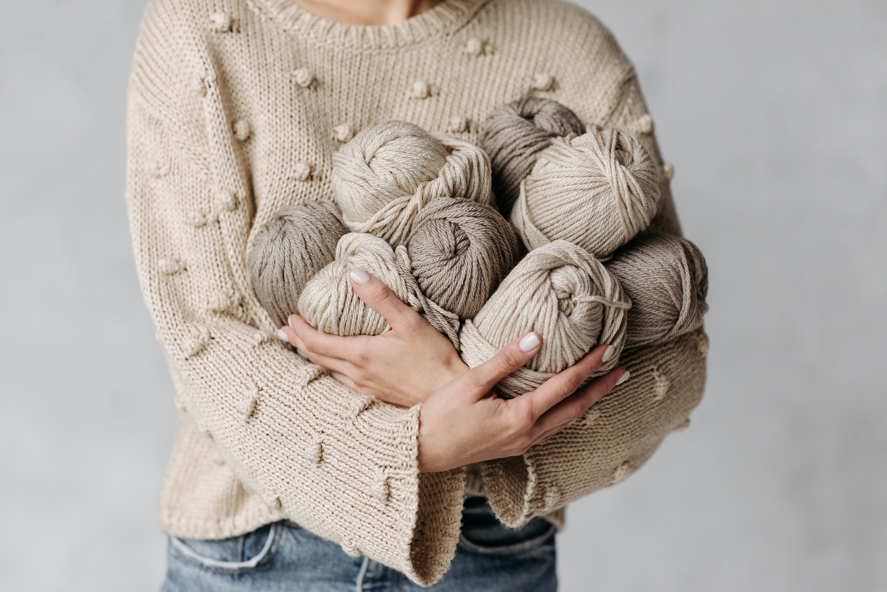 A Person in Beige Knitted Sweater Holding Yarns